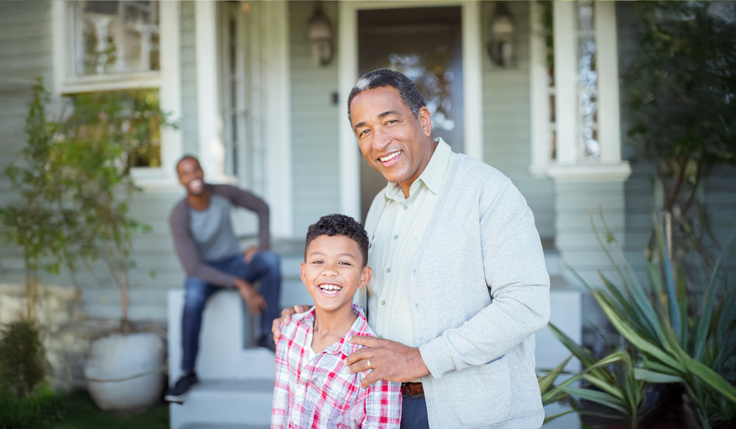 retired man and grandson with son in background in front of home